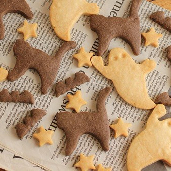 英字新聞の上に広げられたおばけ、猫、コウモリ、星の形のクッキー（プレーンとココアの2種類）