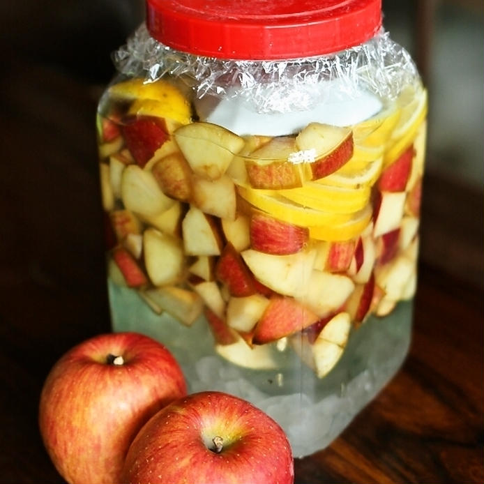 りんごとレモン、氷砂糖、ホワイトリカーが入った保存瓶と赤いりんごの実
