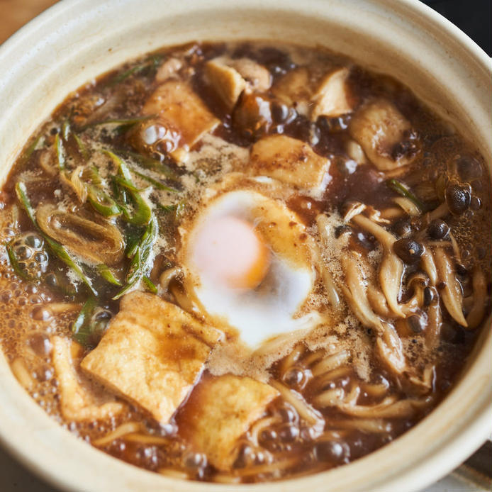 クリーム色の器に盛られた鶏もも肉や油揚げなどの味噌煮込みうどん