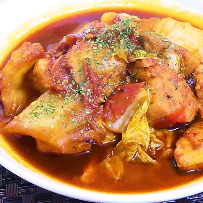 白いお皿に盛り付けられた鶏むね肉と白菜のトマト煮が、黒いラタンテーブルの上に置かれている様子