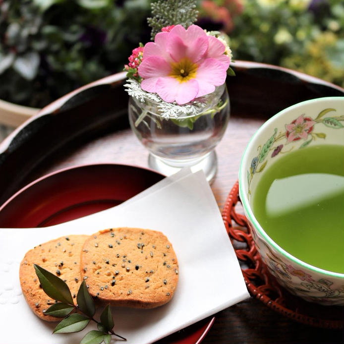 和風の皿に盛りつけられた黒ごまきなこクッキーにお茶と花が添えられている