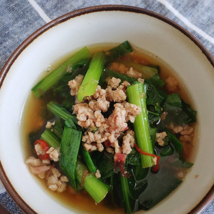 茶色い縁取りの器に盛りつけられた小松菜とひき肉のもつ煮風スープ