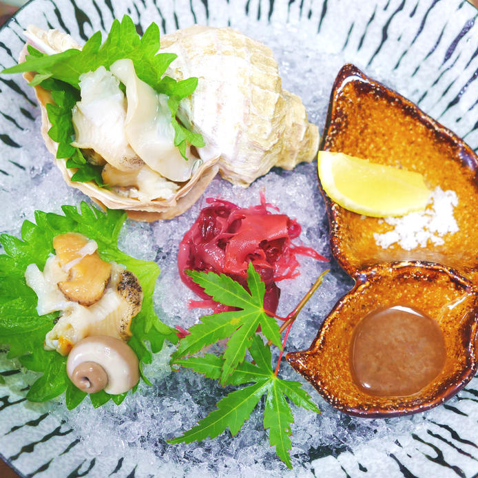 和食器につぶ貝の刺身が盛られ、その横にはレモンや塩が添えられている