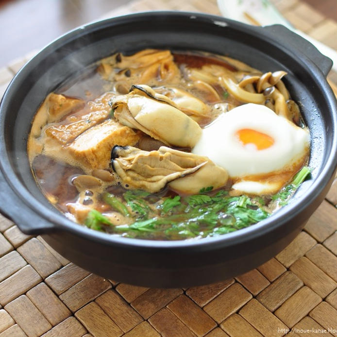 黒い土鍋に盛られた生かき（加熱用）と卵などの味噌煮込みうどん