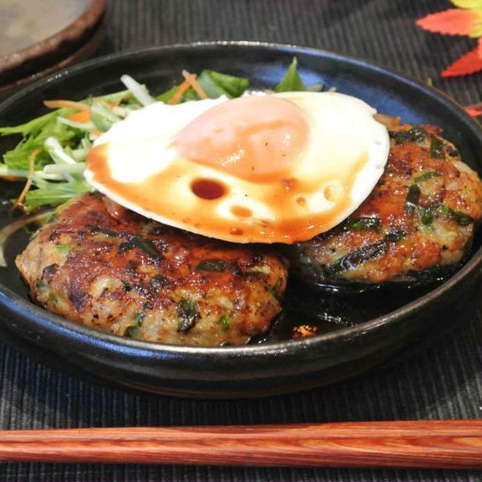 黒い皿に盛りつけられている、照り焼きニラハンバーグと目玉焼き