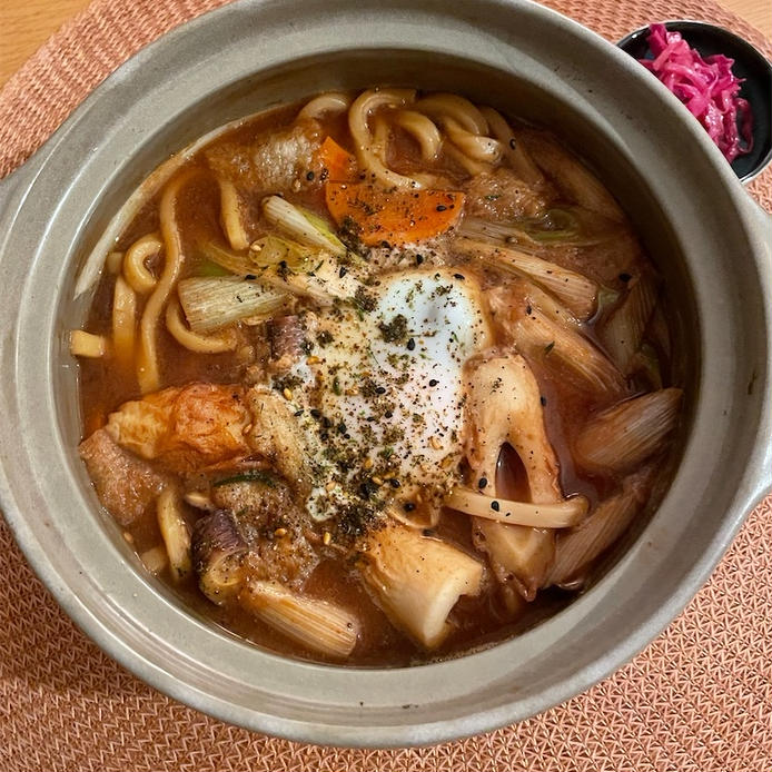 グレーの土鍋に盛られた鶏むね肉やちくわなどの味噌煮込みうどん