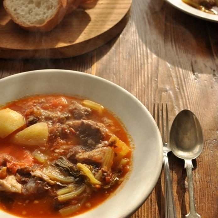 トマト色の牛すじスープを盛ったお皿とパンが置かれたテーブル