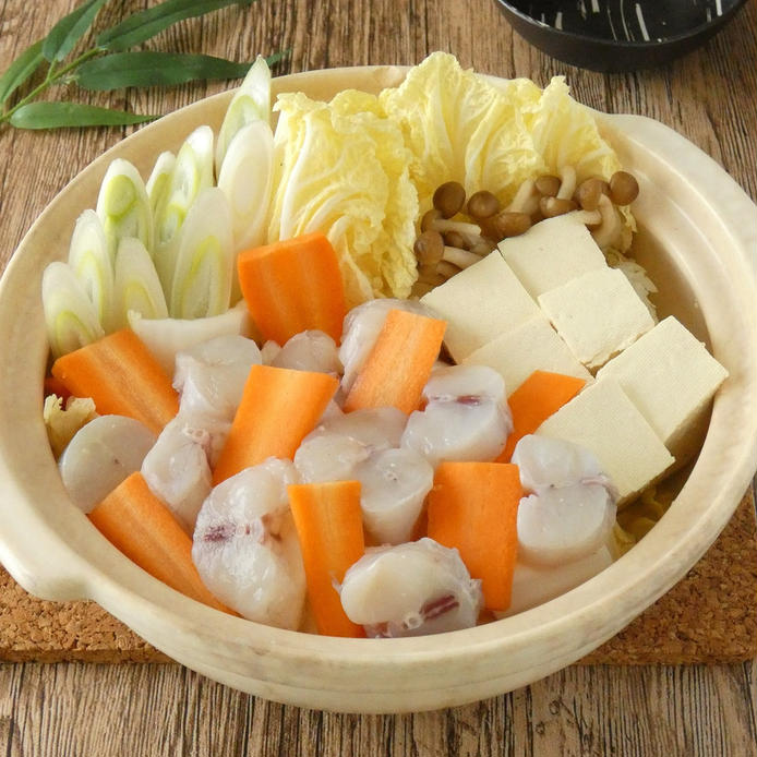 白い土鍋に入っている骨付きフグの身、豆腐やいろんな野菜