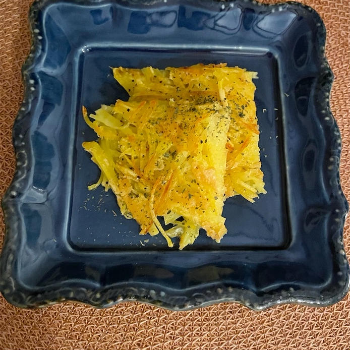 紺色の四角い皿に盛り付けられた、切り分けられたカレー粉ととろけるチーズ入りのじゃがいもガレット