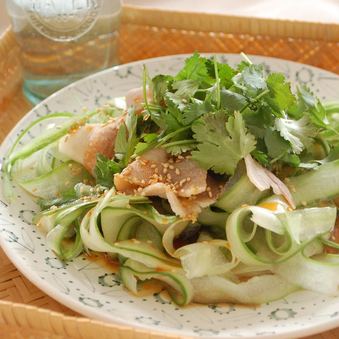 緑の模様が入った白い皿にのった、豚しゃぶときゅうりとパクチーのサラダ