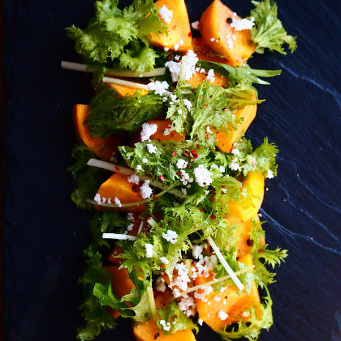 黒いフラット皿に盛り付けた柿の彩りグリーンサラダ