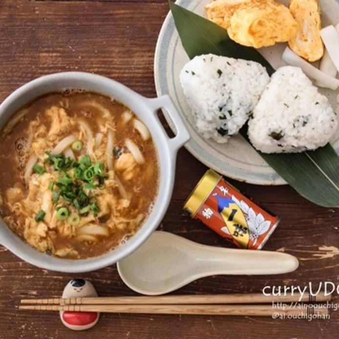 白い土鍋に入っているおそば屋さんのカレーうどんとおにぎりなど