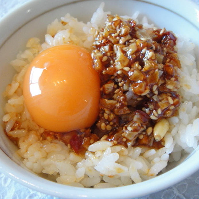 白い茶碗に盛られた食べるラー油のせ卵かけご飯がレースマットの上に置かれている様子