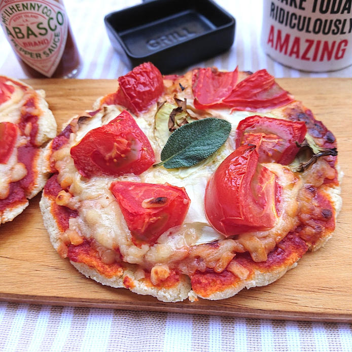 縦縞のテーブルクロスの上の木の板にトマトのピザがのっている。