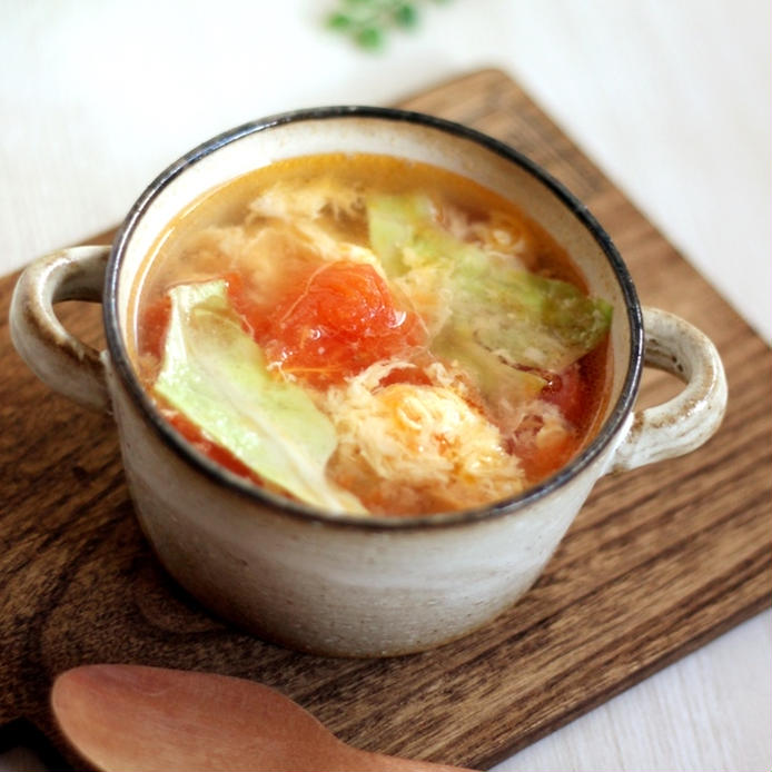 ベージュのスープカップにトマトとレタスと卵のスープが入っており、手前には木のスプーンが添えられている