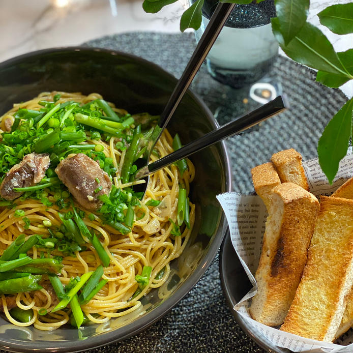 黒い丸皿に盛られたししとうとオイルサーディンのパスタと食パンが並んだテーブル